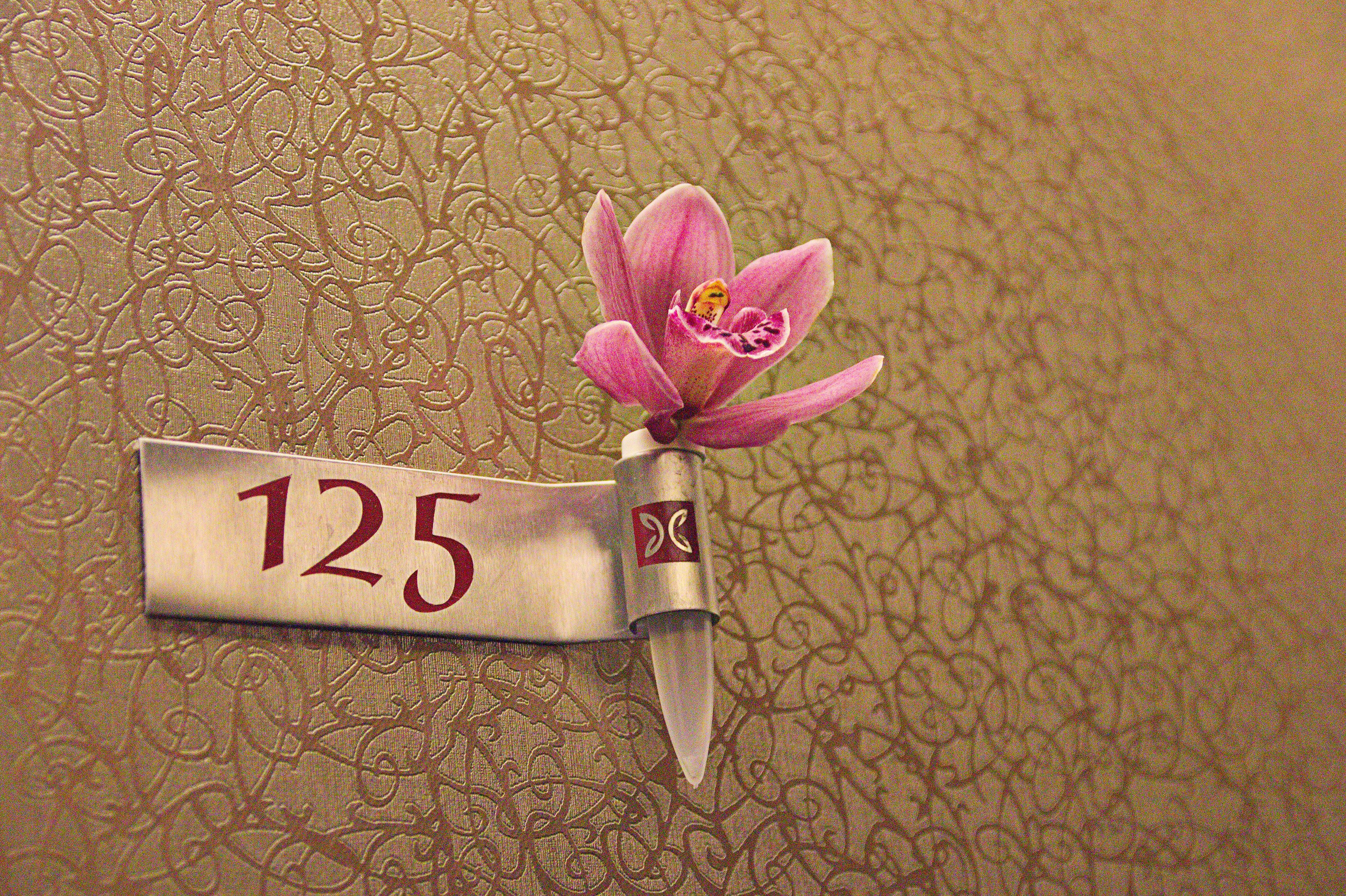 A room number sign with a decorative flower and a small emblem.