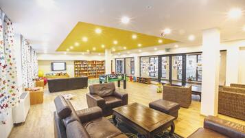 A spacious lobby with leather sofas, a coffee table, and a bookshelf.