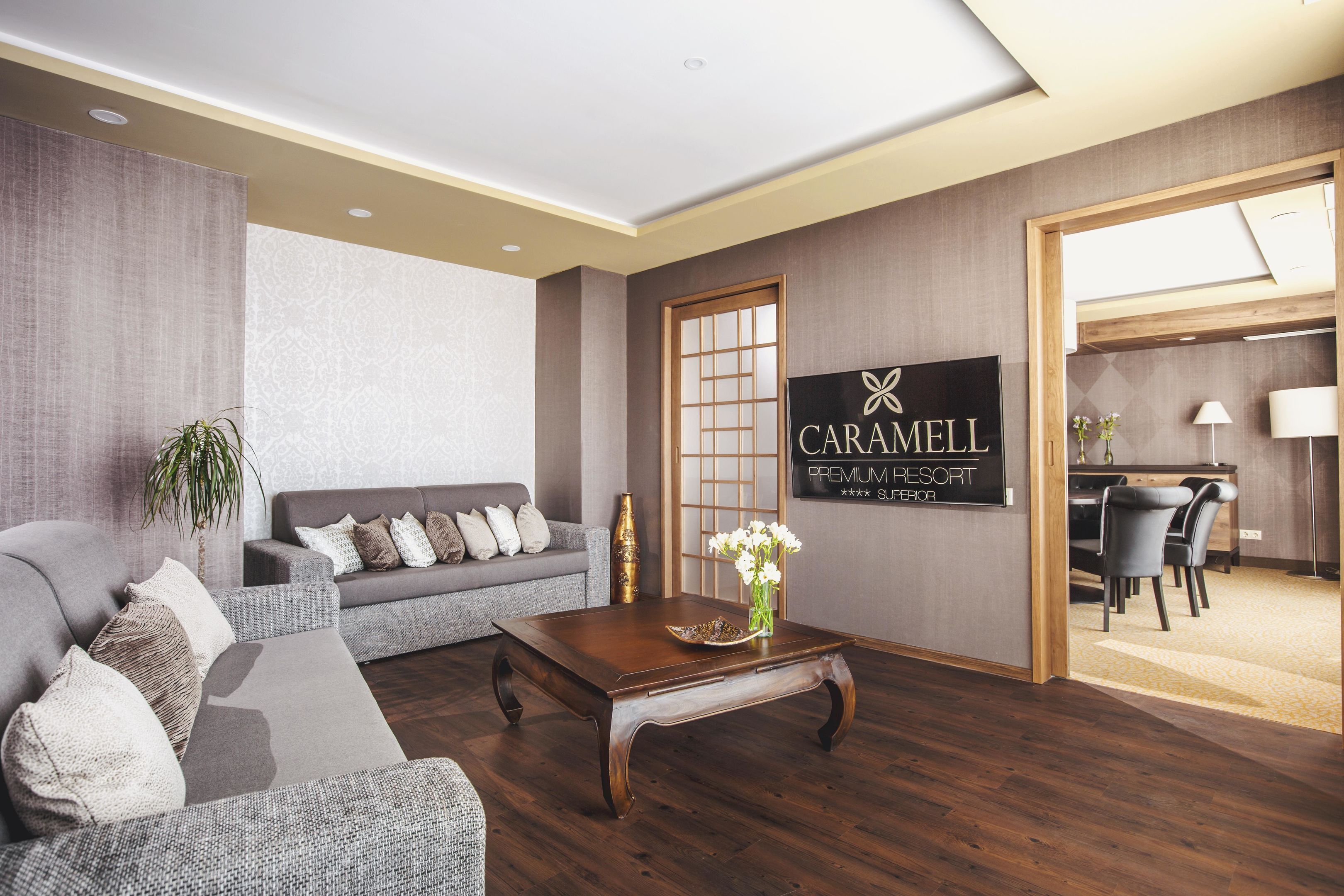 Una sala de estar moderna con un sofá gris, una mesa de centro de madera y un cartel de Caramel Premium Resort.