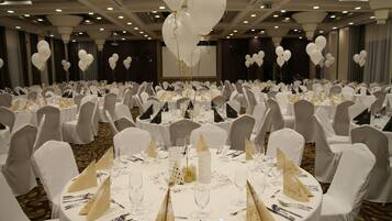 A banquet hall with round tables set for a formal event, featuring white tablecloths, gold centerpieces, and white chairs.