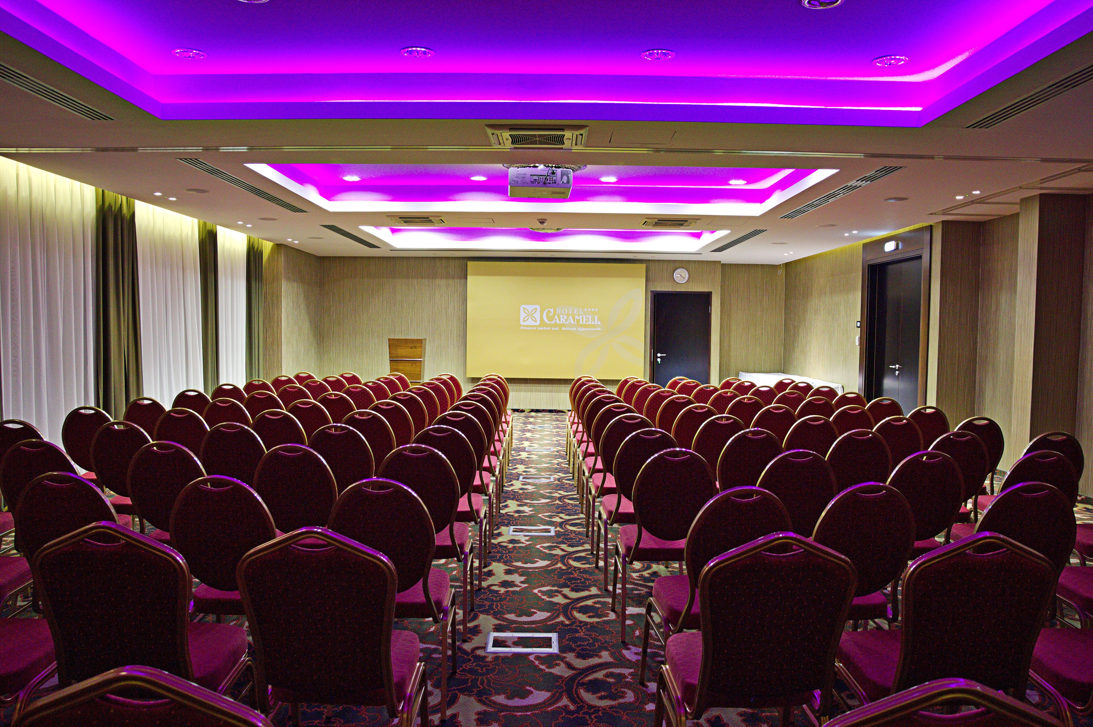 A conference room with rows of red chairs, a carpeted floor, and a projector screen at the front.
