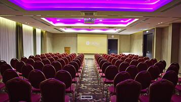 A conference room with rows of red chairs, a carpeted floor, and a projector screen at the front.
