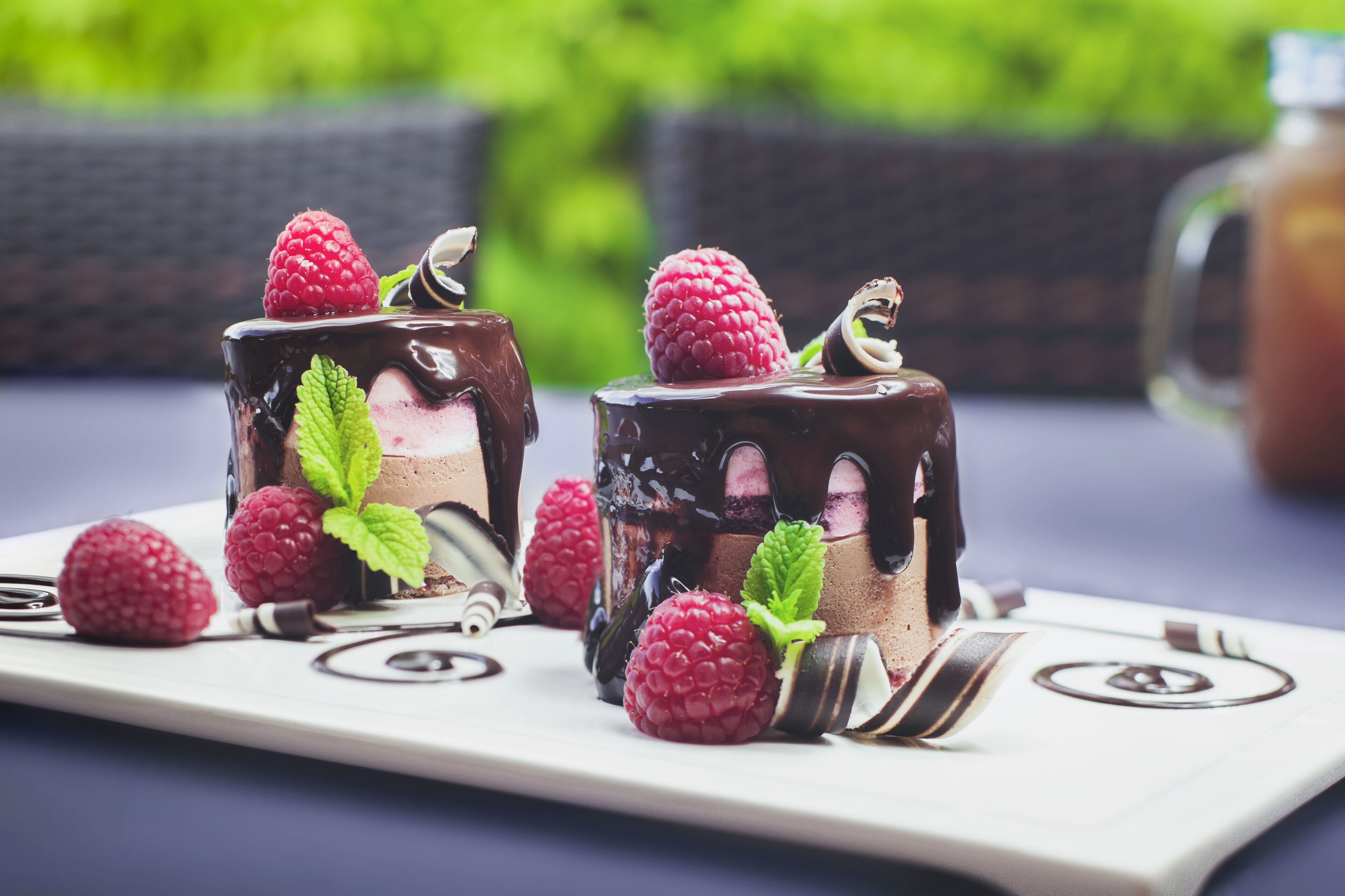 Two chocolate-topped desserts with raspberries and mint leaves on a white plate.