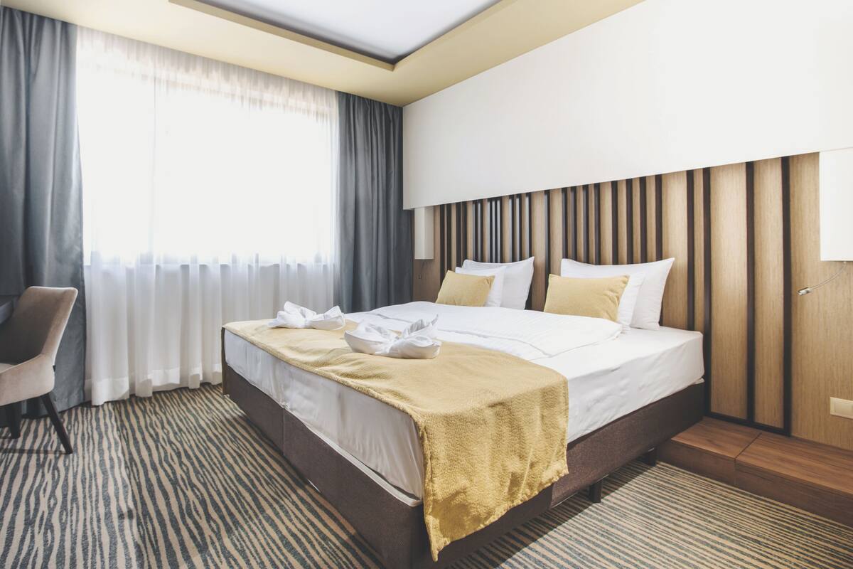 Ein modernes Hotelzimmer mit einem großen Bett, einem Sessel, einem Schreibtisch und einem Fenster mit Vorhängen.