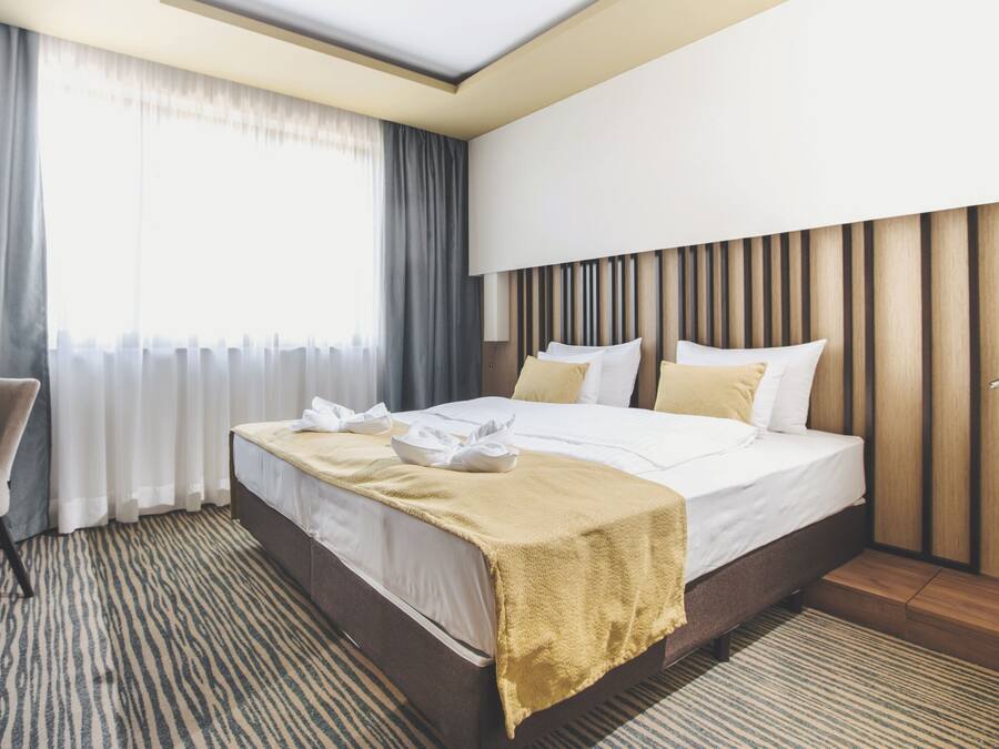 Una habitación de hotel moderna con una cama grande, una silla, un escritorio y una ventana con cortinas.