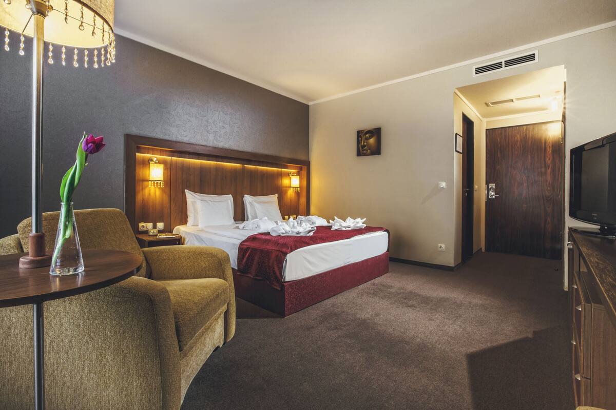 Ein Hotelzimmer mit einem Bett, einem Sessel, einem Tisch, einem Fernseher und einer Lampe.