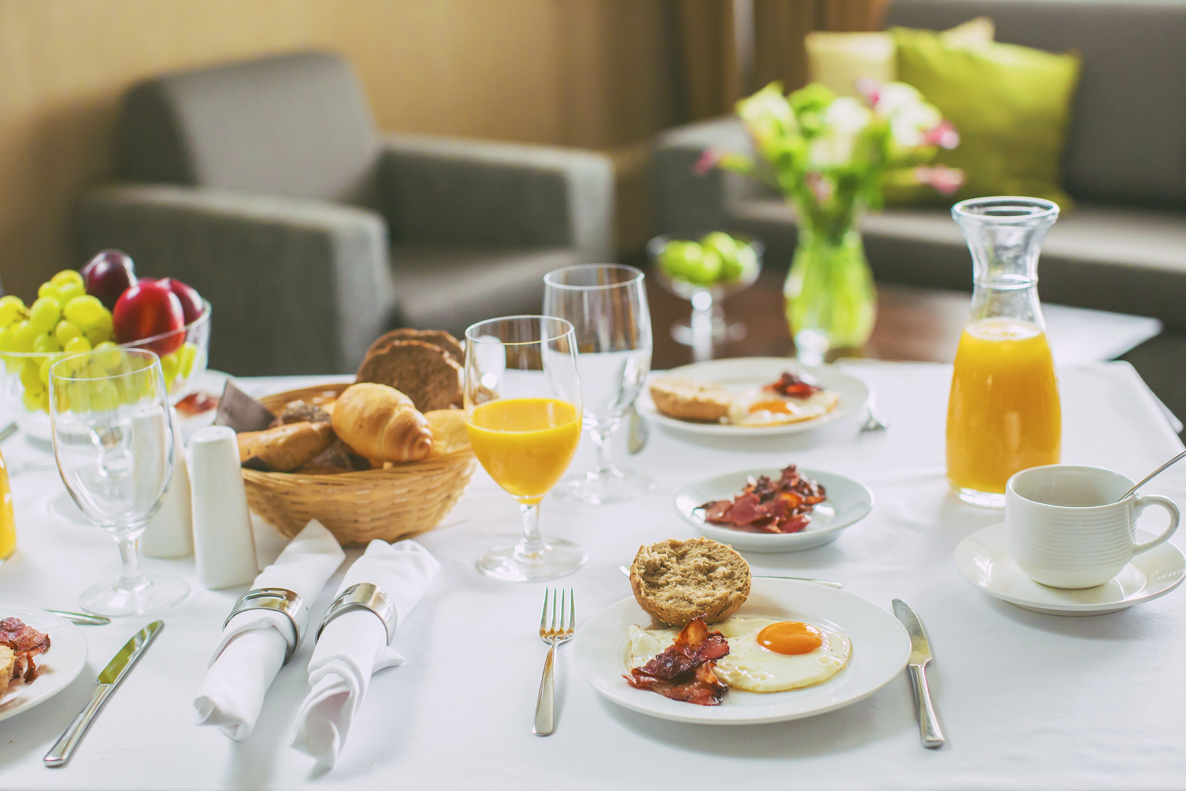 A breakfast table with various food items, including eggs, bacon, toast, and fruit.