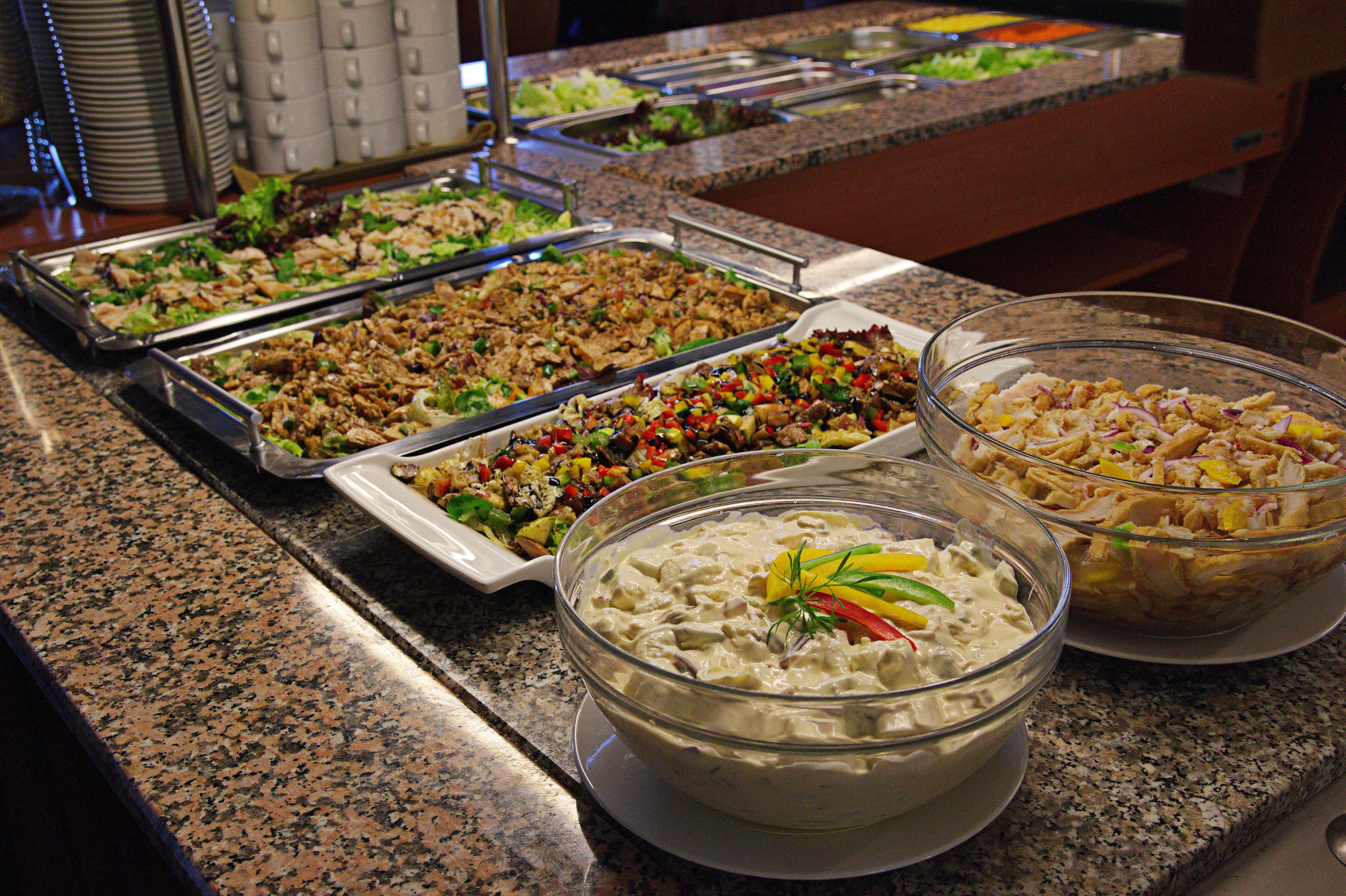 Ein reichhaltiges Buffet mit verschiedenen Speisen, darunter Salate, Fleischgerichte und eine große Schüssel cremiger Dip.