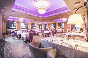 A spacious dining area with multiple tables and chairs, large windows, and a modern ceiling design. - Caramell Premium Resort (Buk)