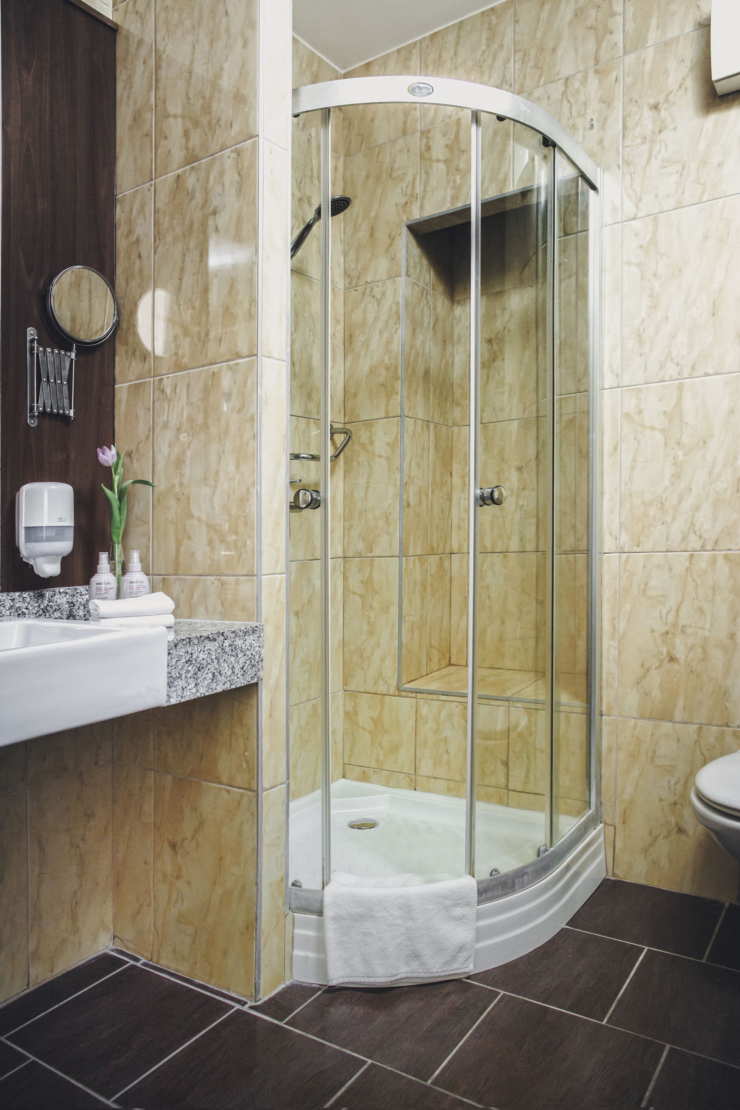 A modern bathroom with a glass-enclosed shower, a marble-tiled wall, a sink with a marble countertop, and a toilet.