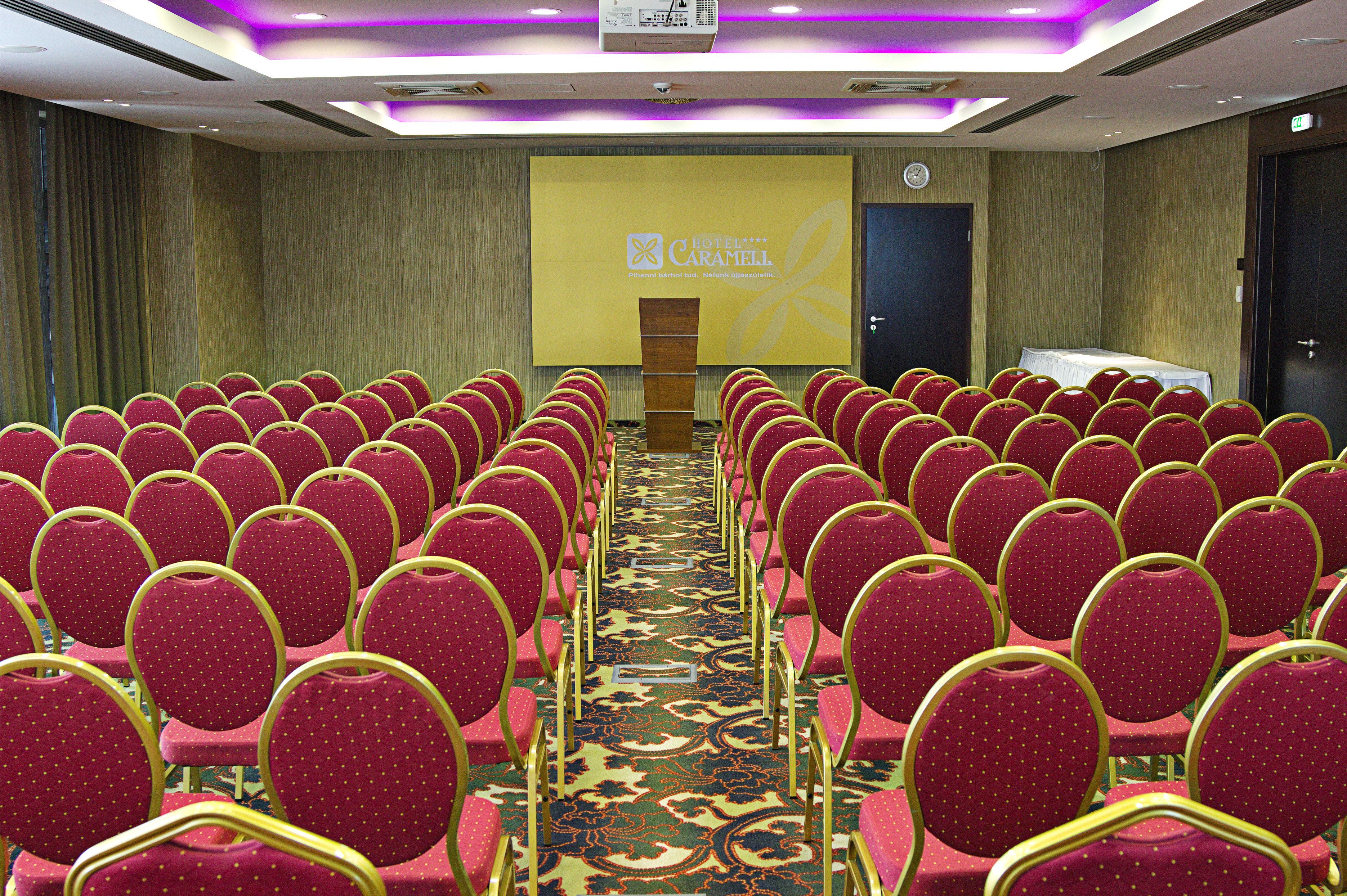 Una sala de conferencias con hileras de sillas rojas y suelo alfombrado.