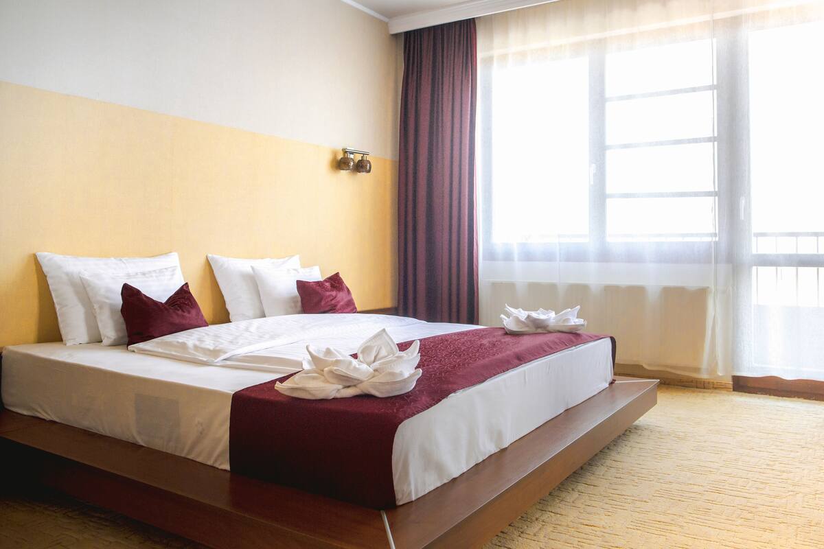 Ein Hotelzimmer mit einem großen Bett, Holzboden und einem Vorhangfenster.