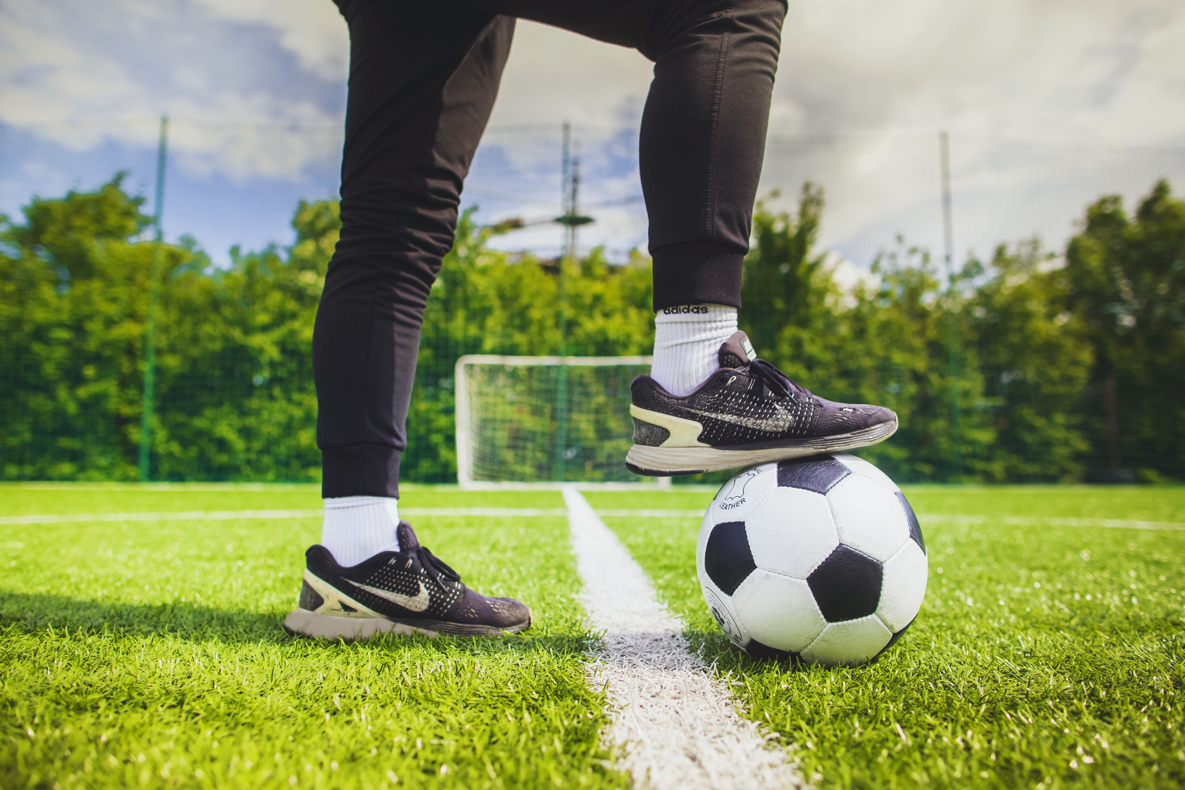 Una pelota de fútbol sobre un campo de césped con un arco de portería al fondo.