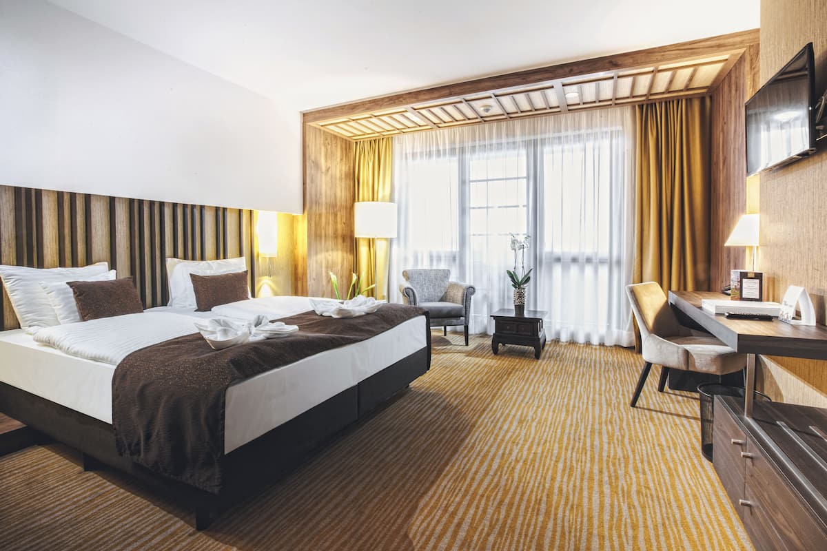 Ein Hotelzimmer mit einem großen Bett, einem Schreibtisch, einem Sessel und einem Fernseher.
