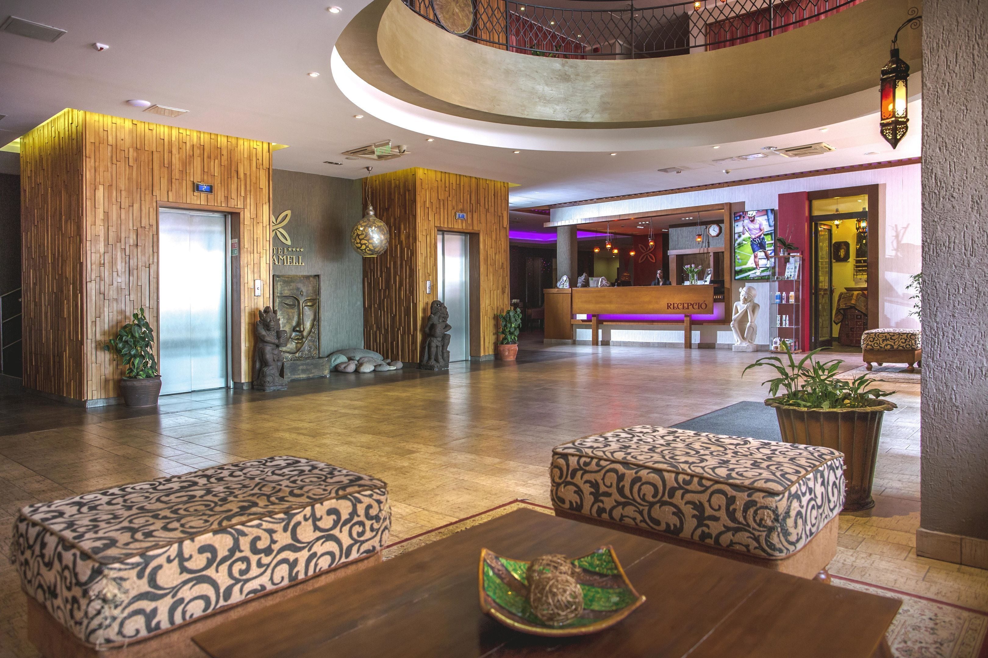 Een hotel lobby met een receptiebalie, twee gestreepte banken, een wachtruimte met een televisie en een trap naar een hoger gelegen verdieping.