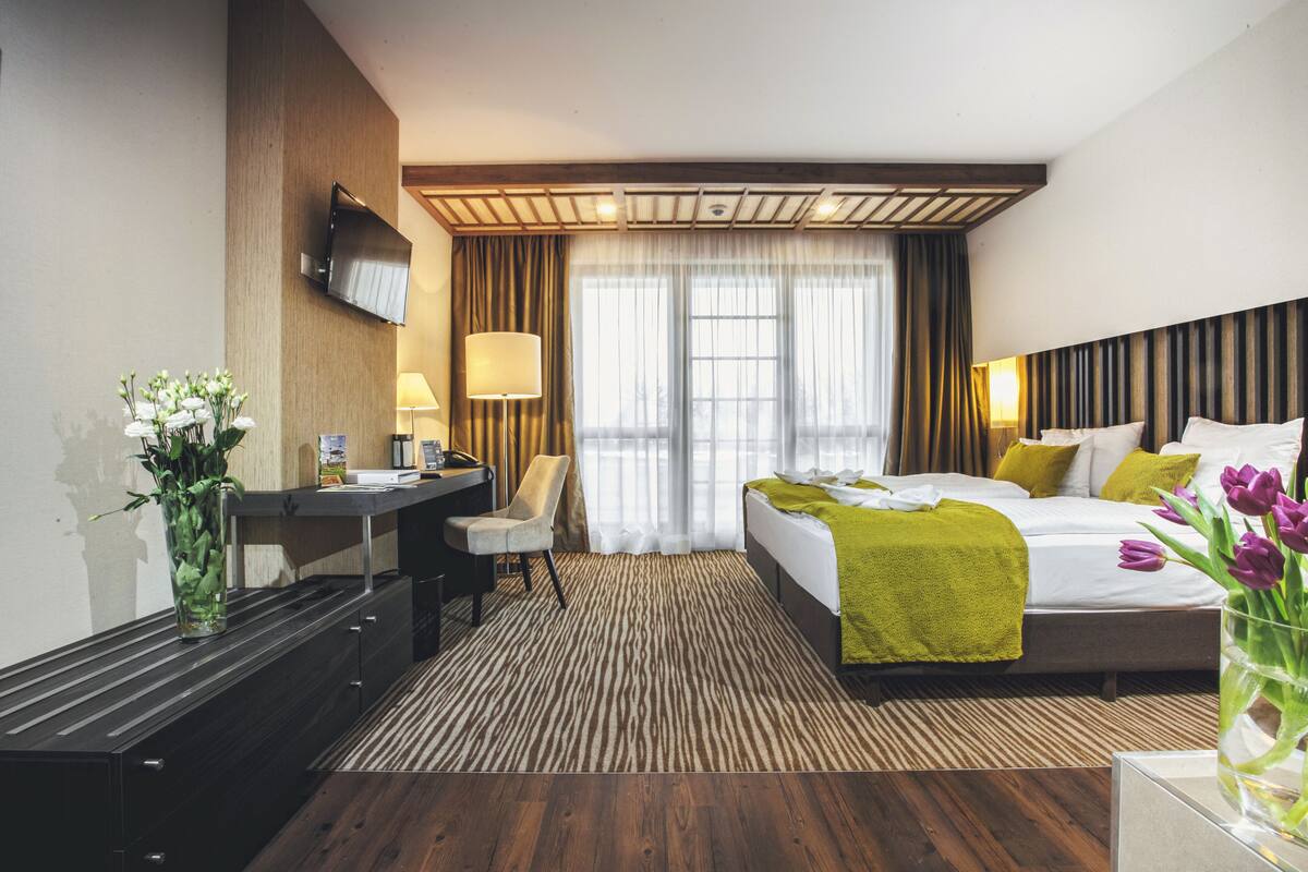 Ein Hotelzimmer mit Bett, Schreibtisch, Stuhl, Fernseher und einem Fenster mit Vorhängen.