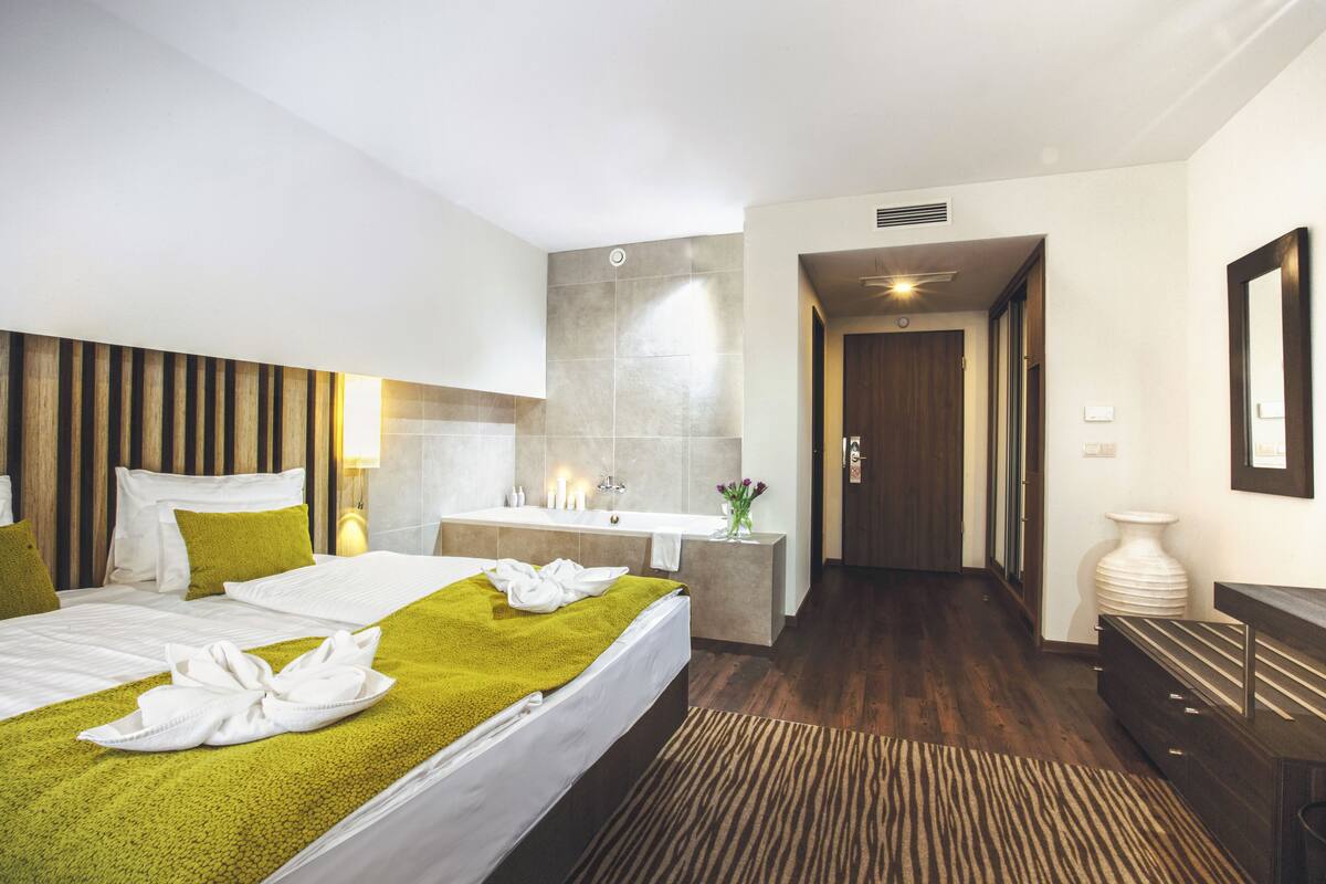 Ein modernes Hotelzimmer mit einem großen Bett, einem Badezimmer mit Waschbecken und Spiegel sowie einem Holzboden.