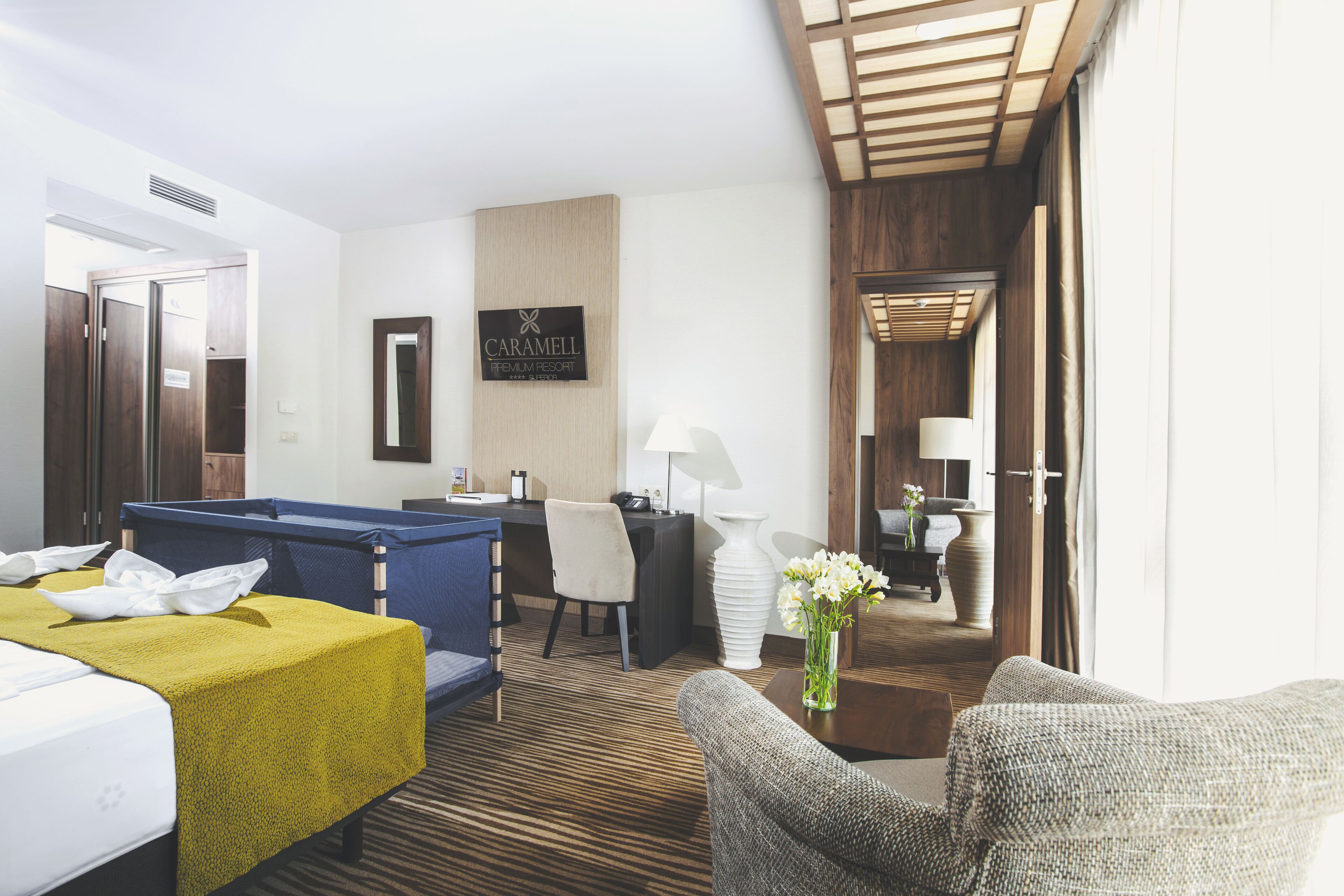 A hotel room with a bed, a desk, a chair, a sofa, a lamp, and a vase with flowers.