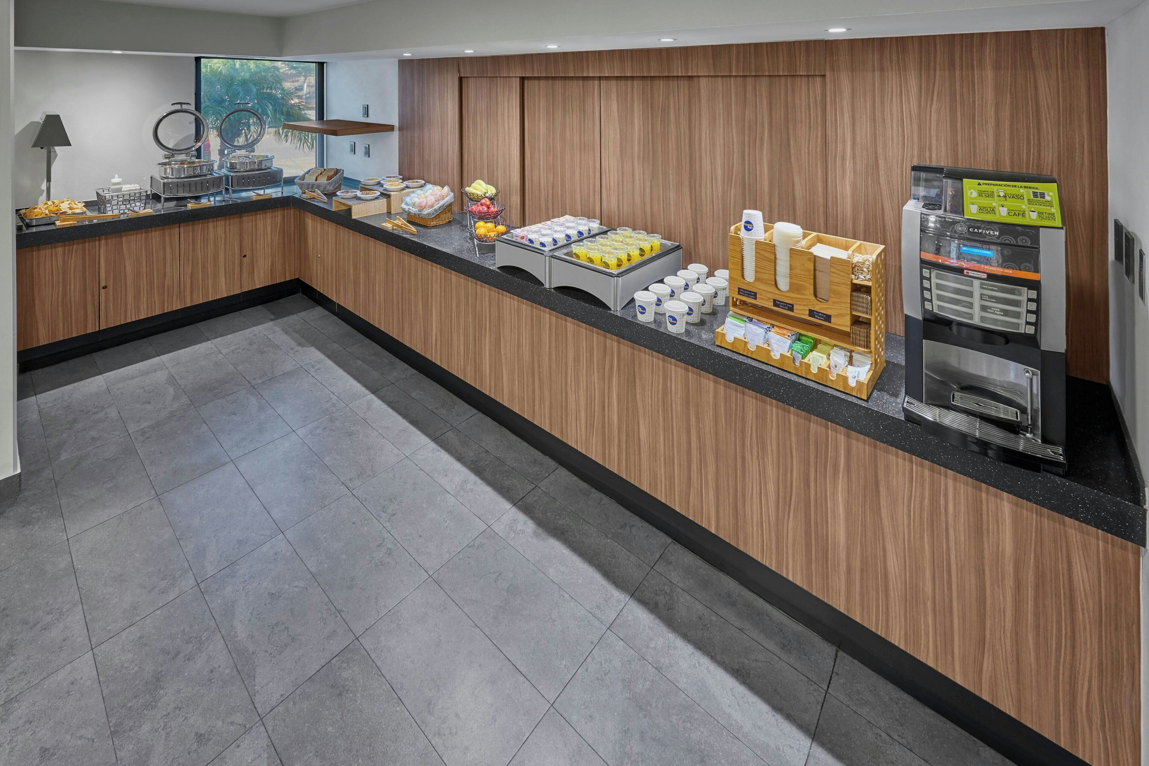 A modern breakfast area with a wooden counter, a coffee machine, and various food items.