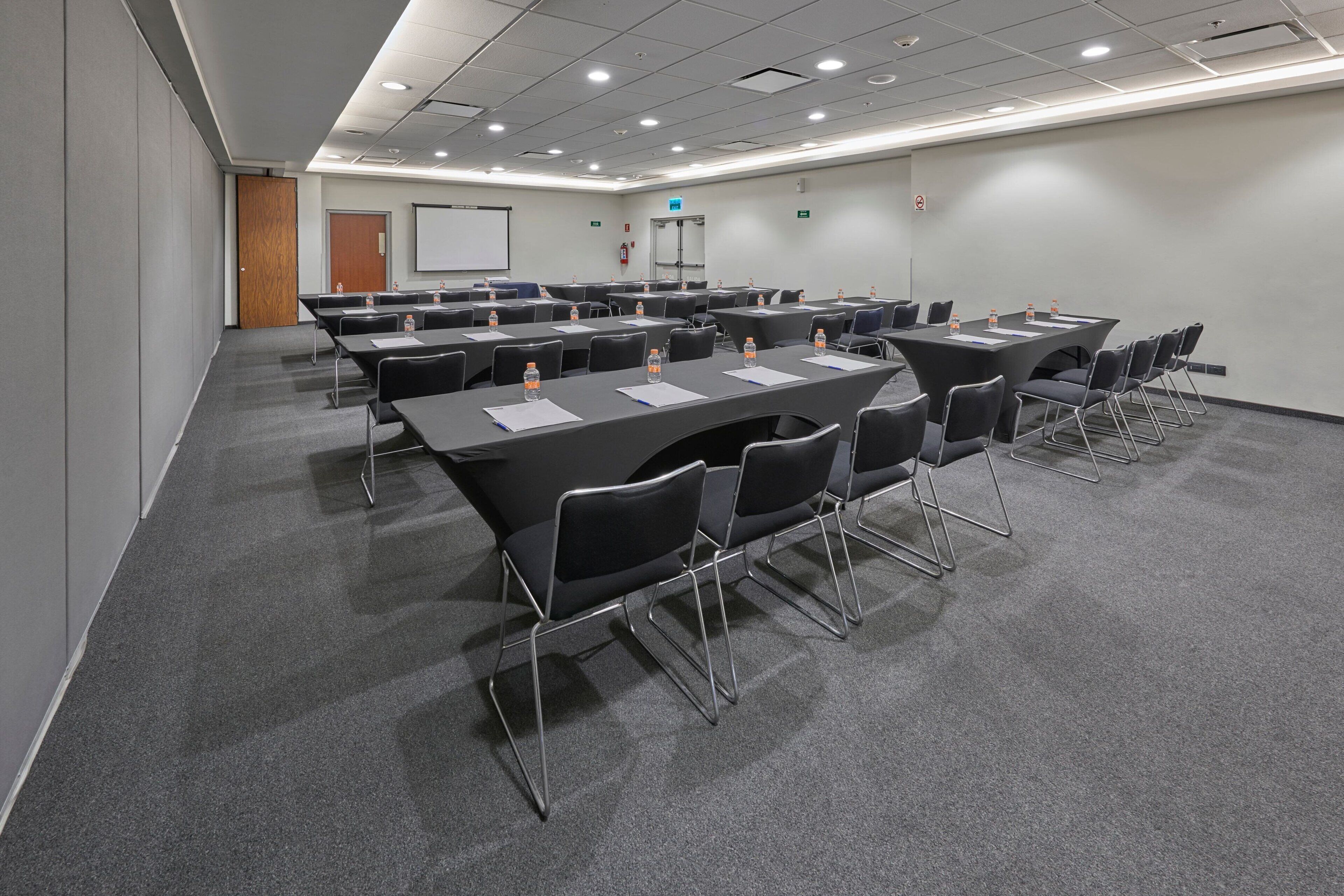 A conference room with multiple tables and chairs, equipped with water bottles and papers.