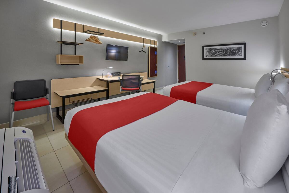 Quarto de hotel com duas camas, uma escrivaninha, uma cadeira, uma televisão e um aquecedor.