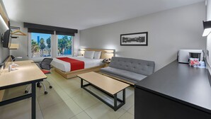 Ein modernes Hotelzimmer mit Bett, Sofa, Schreibtisch und Blick auf Palmen.