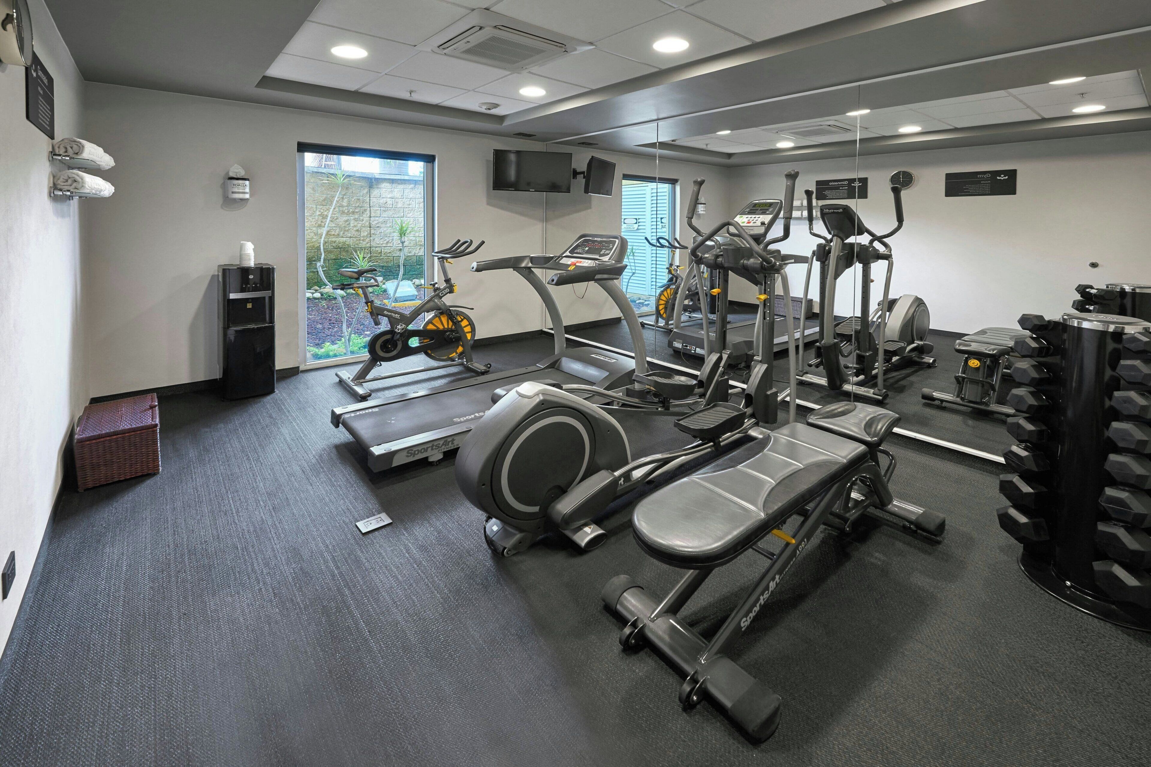 A modern gym with cardio machines, free weights, and a water station.