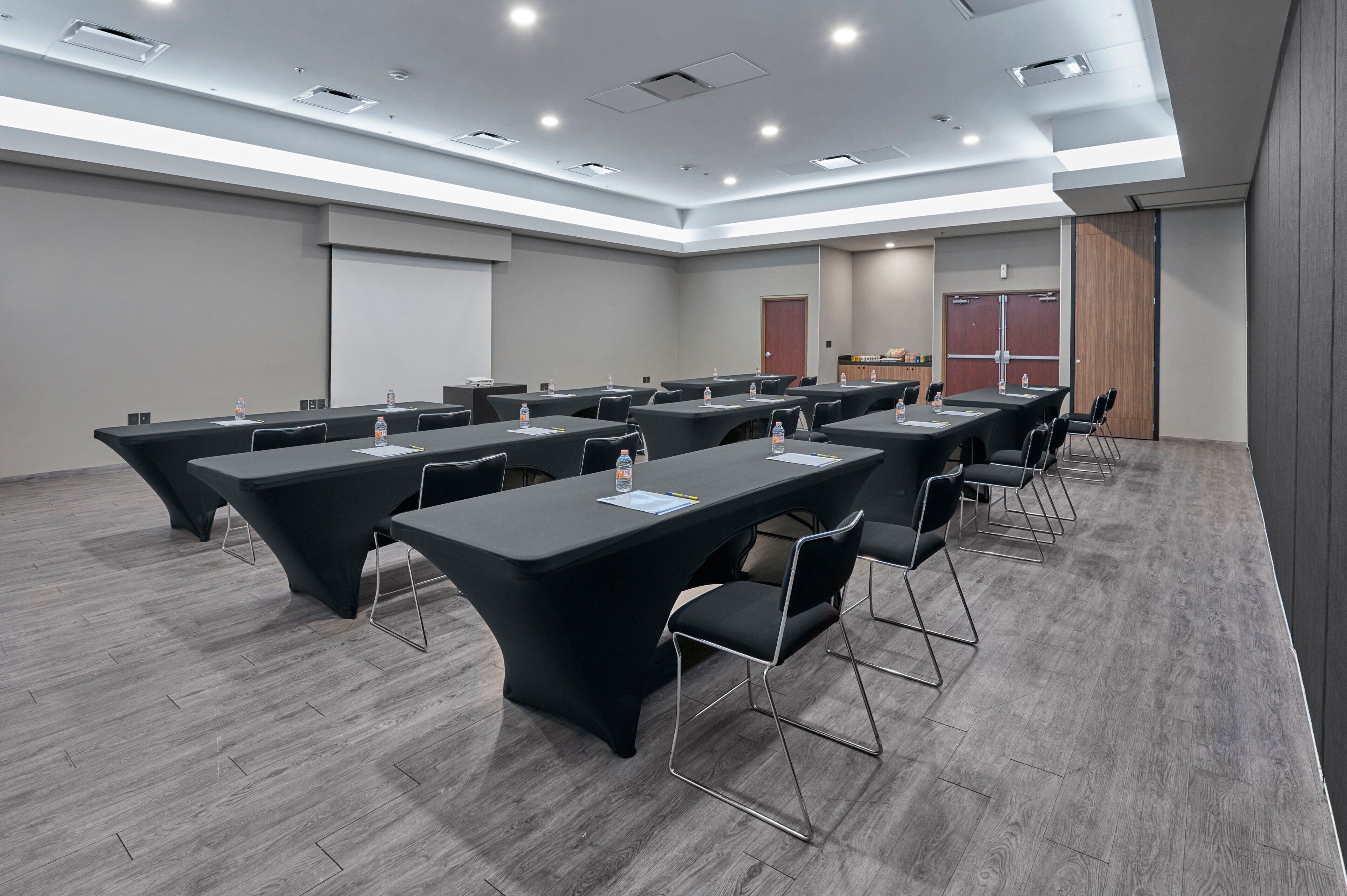 A conference room with long tables, chairs, and a projector screen.