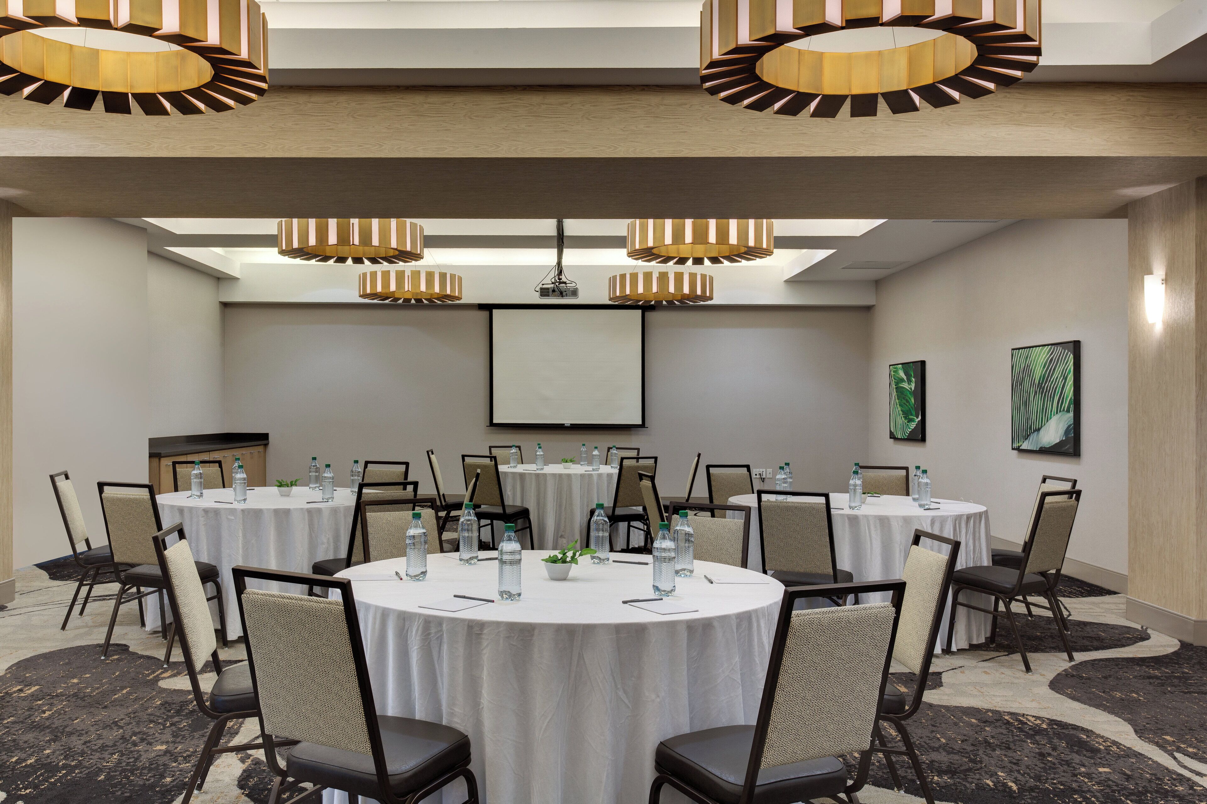 A conference room with round tables, chairs, and modern pendant lighting.