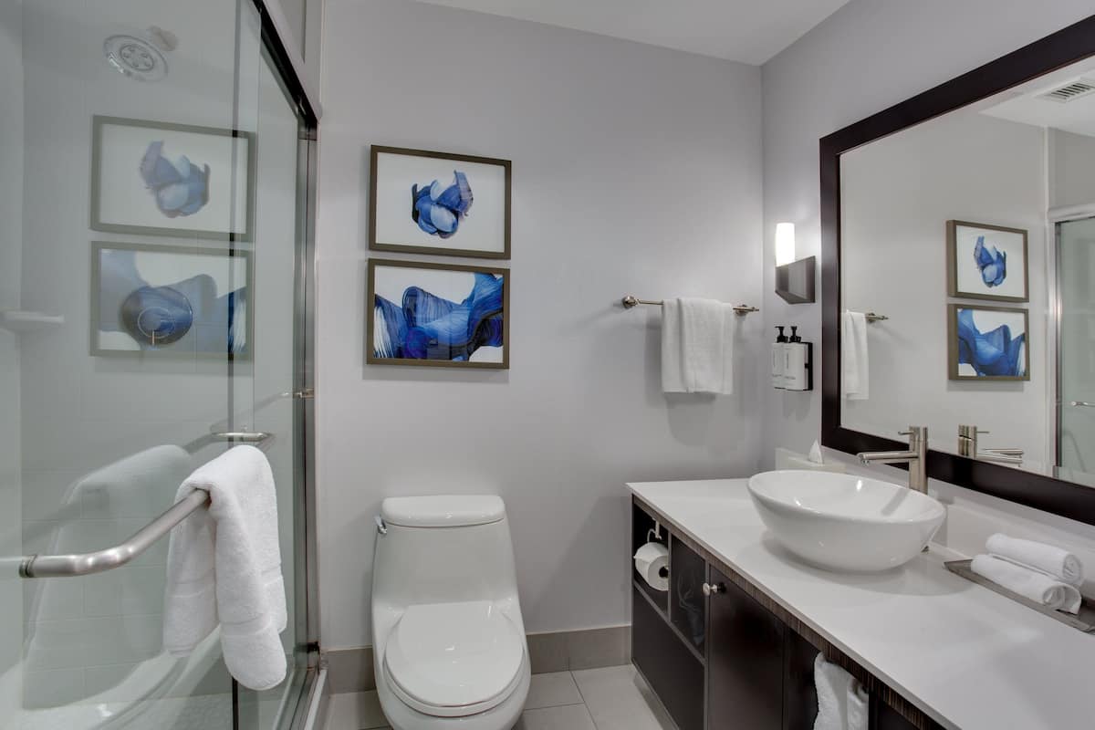 Ein modernes Badezimmer mit Duschkabine aus Glas, einer weißen Toilette, einem großen Waschbecken und drei gerahmten, blauen abstrakten Bildern an der Wand.