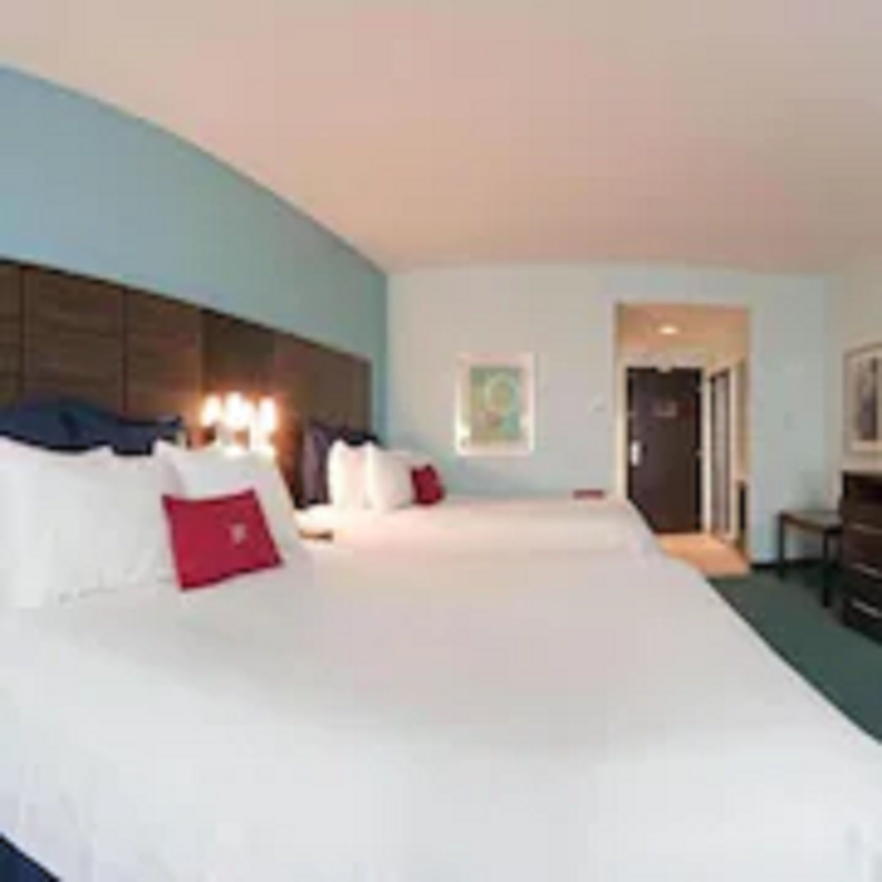 Een hotelkamer met een groot bed, een hoofdeinde, een nachtkastje en een deur naar een andere kamer.
