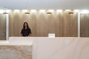 A reception desk with a marble counter, wooden panel wall, and pendant lighting.