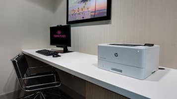 A hotel room with a white desk, a black monitor, a HP printer, and a chair.