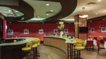 Un interior de restaurante con una barra curva, taburetes amarillos y paredes rojas.