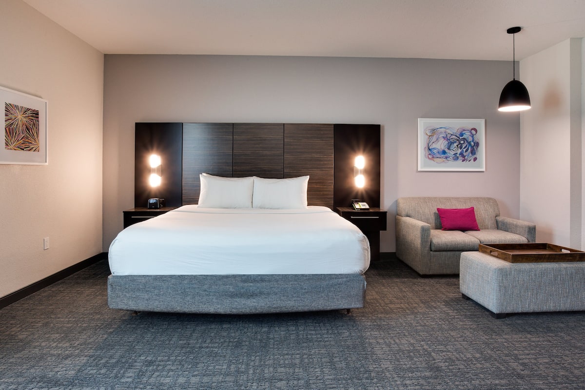 Ein Hotelzimmer mit einem großen Bett, einem Sessel, einem kleinen Tisch und Bildern an den Wänden.