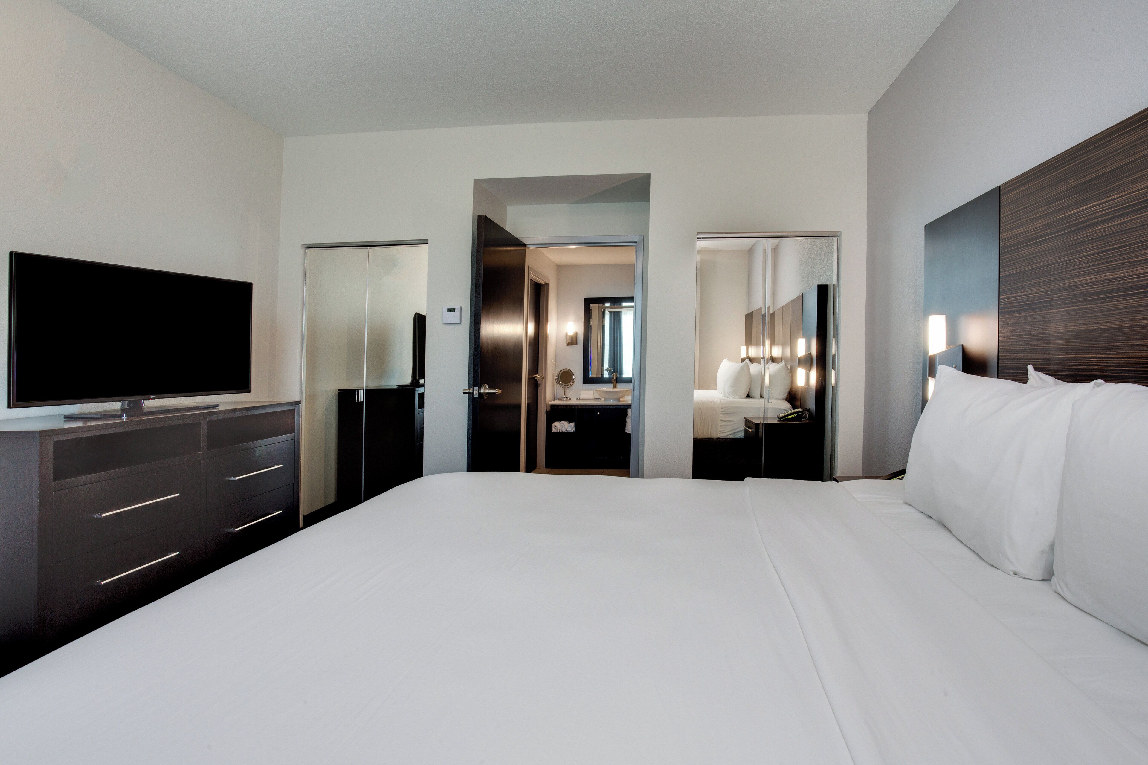 Une chambre d’hôtel moderne, dotée d’un grand lit, d’un téléviseur à écran plat, d’une commode et d’une salle de bain visible à travers une porte ouverte.