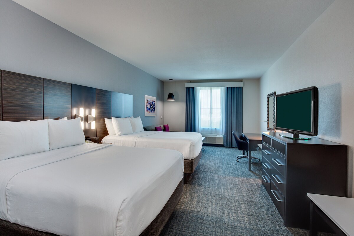 A hotel room with two beds, a desk, a television, and a window with curtains.