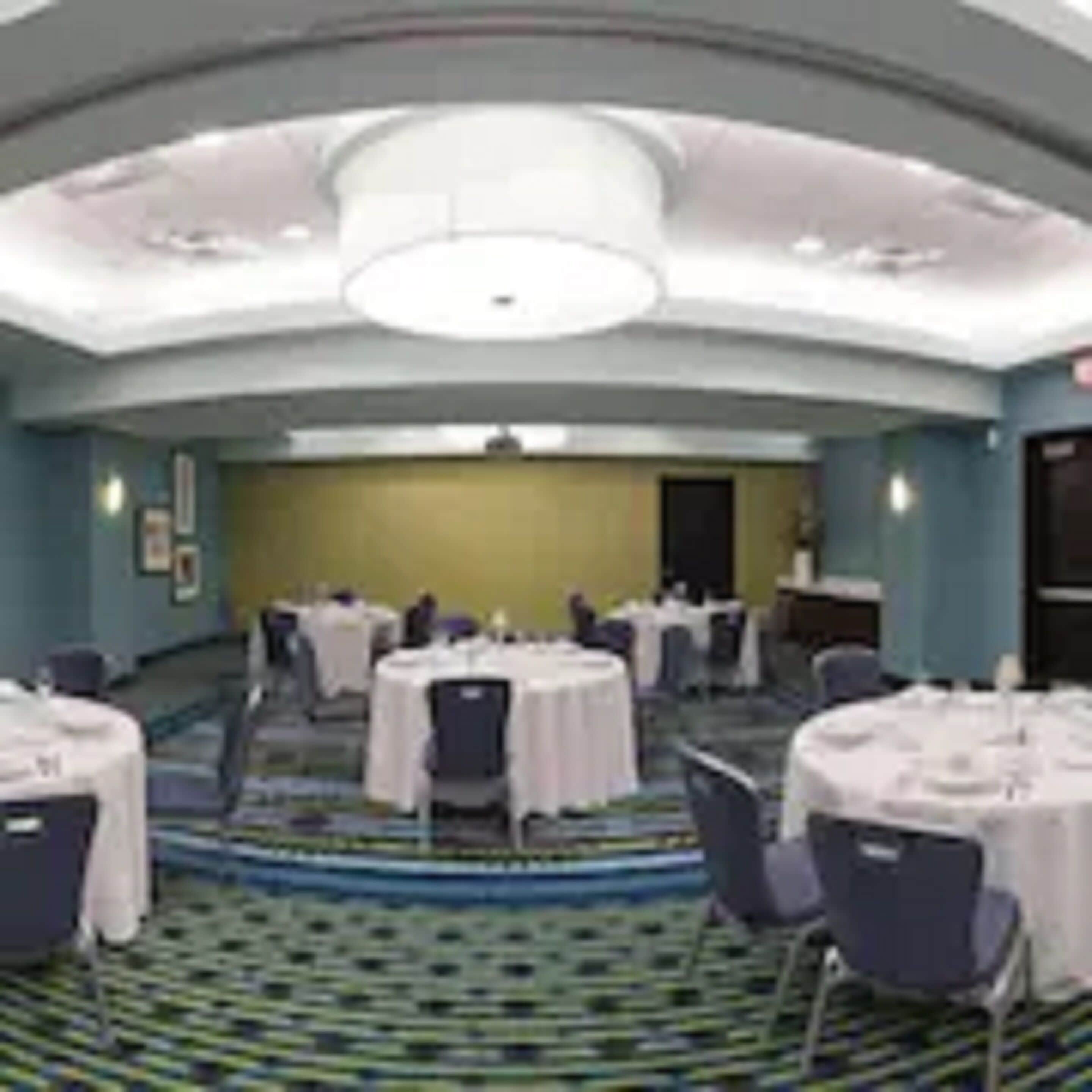 Un salón de conferencias con mesas redondas, sillas y suelo alfombrado.