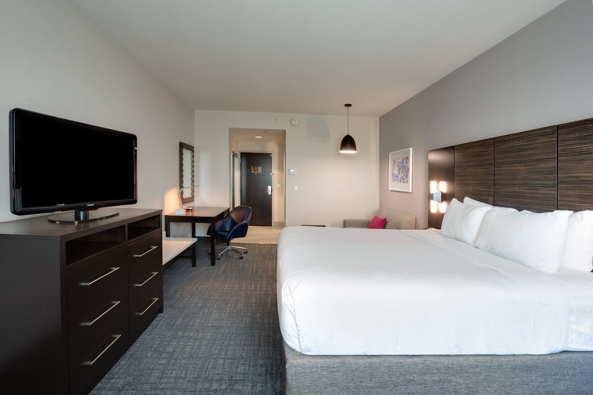 Ein Hotelzimmer mit einem großen Bett, einem Schreibtisch mit Stuhl, einem Flachbildfernseher und einer Kommode.