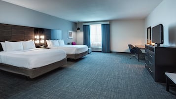 A hotel room with two beds, a desk, a chair, and a television.