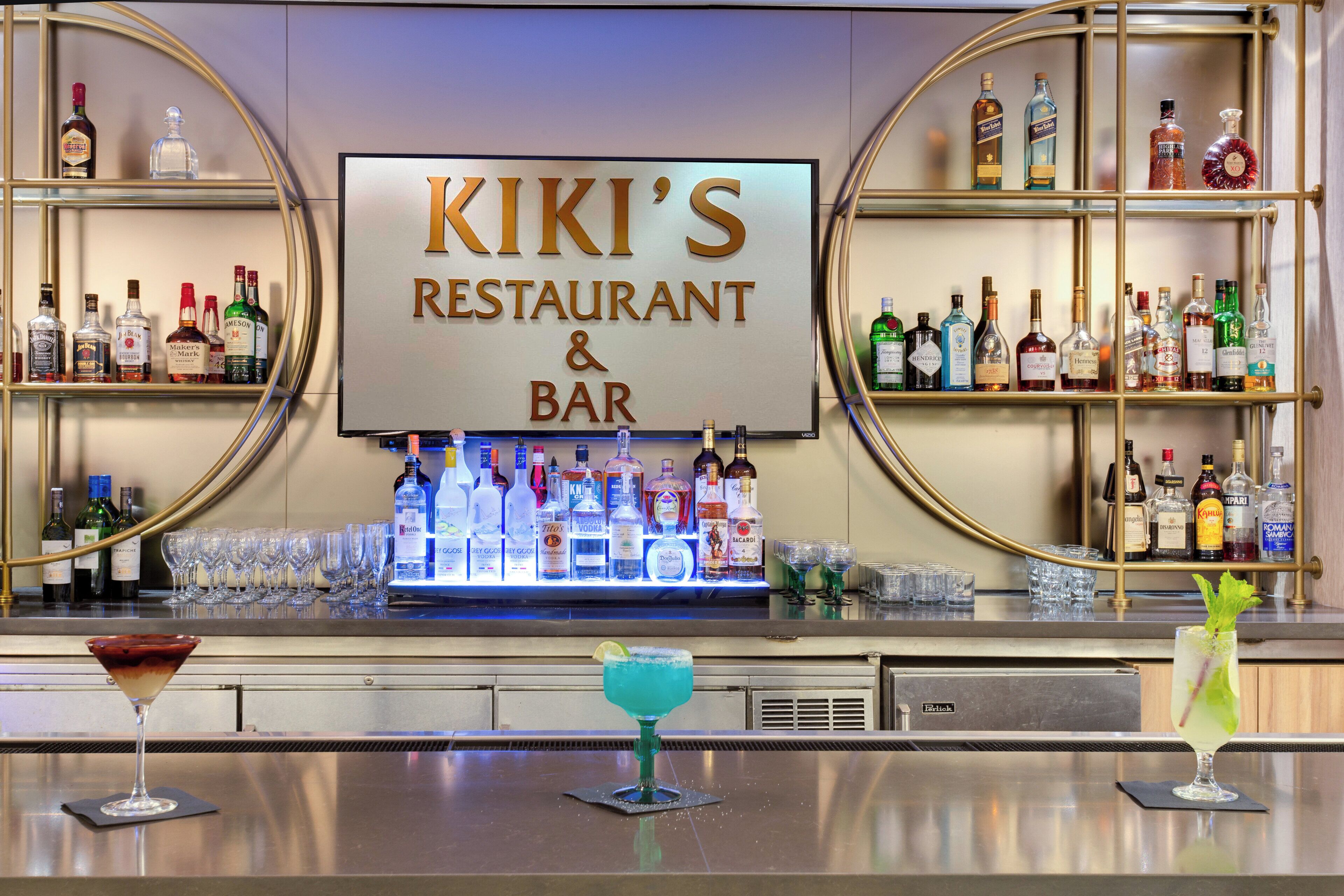 A bar area with a large sign reading 'KIKI'S RESTAURANT & BAR' and shelves stocked with various liquor bottles.