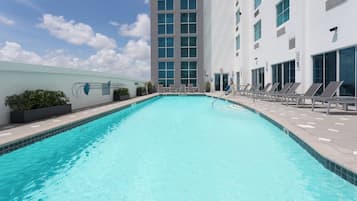 A swimming pool with lounge chairs and a modern building in the background.