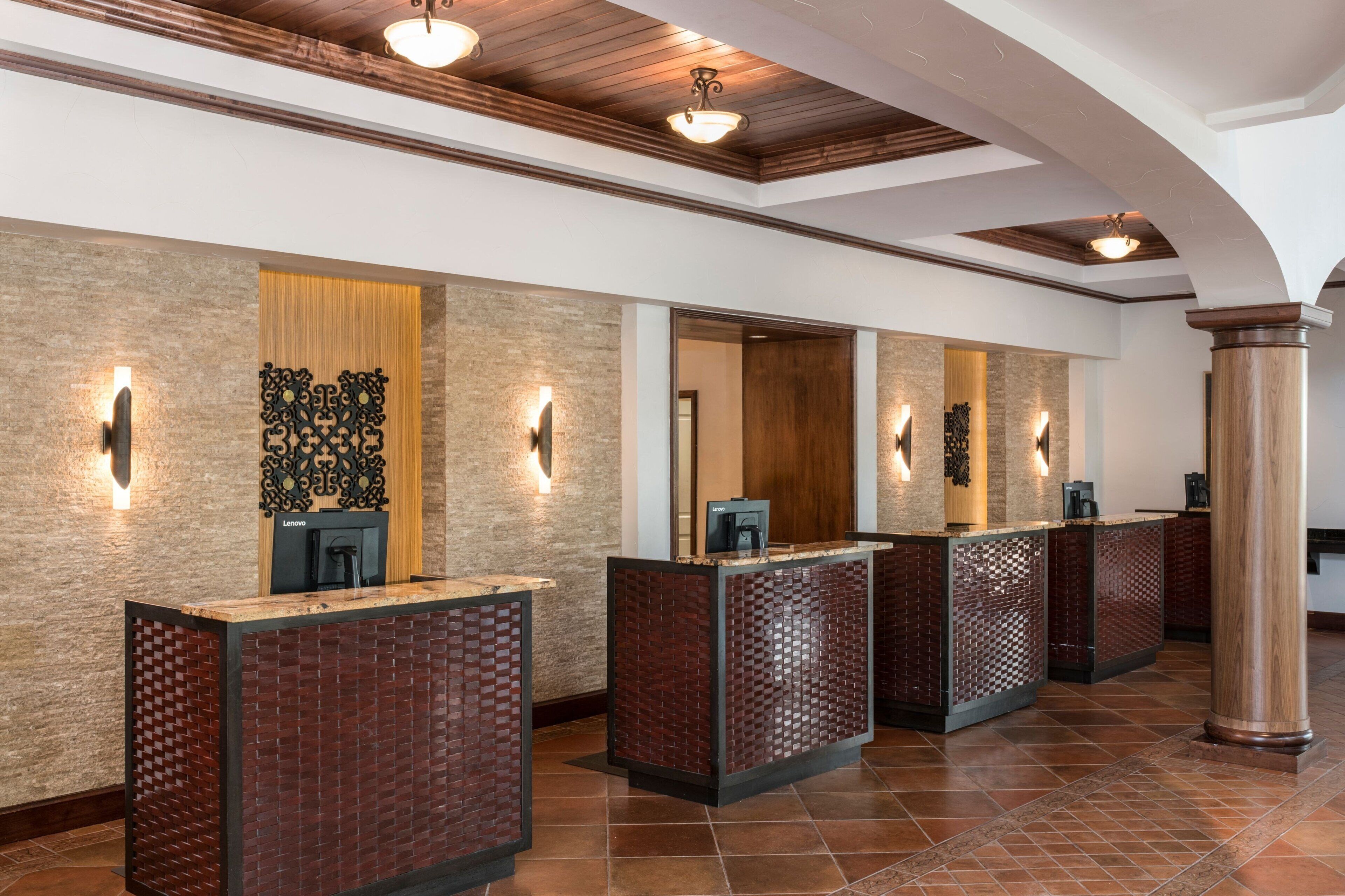 A reception area with three reception desks, each with a computer and a telephone. The walls are textured, and there are decorative wall sconces.