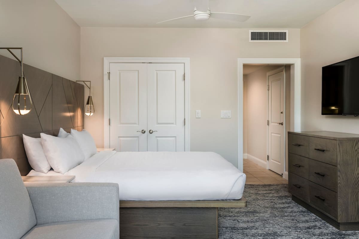 Una camera da letto moderna con un letto, un divano grigio, una cassettiera in legno e una ventola a soffitto.