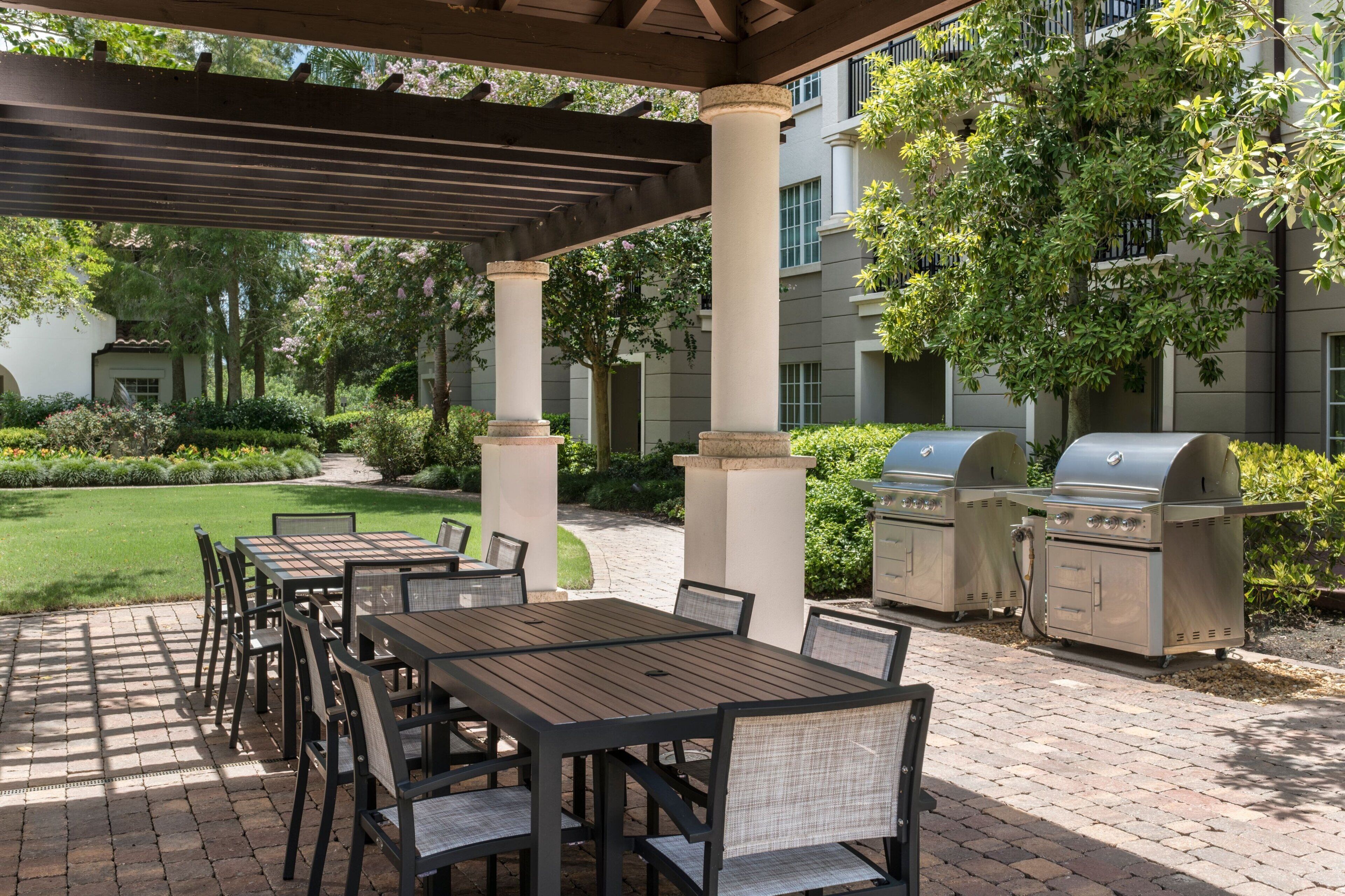 An outdoor patio with tables and chairs, a grill, and a covered area with columns.