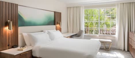 Une chambre d’hôtel moderne, dotée d’un grand lit, d’un bureau, d’une chaise et offrant une vue sur la verdure par la fenêtre.