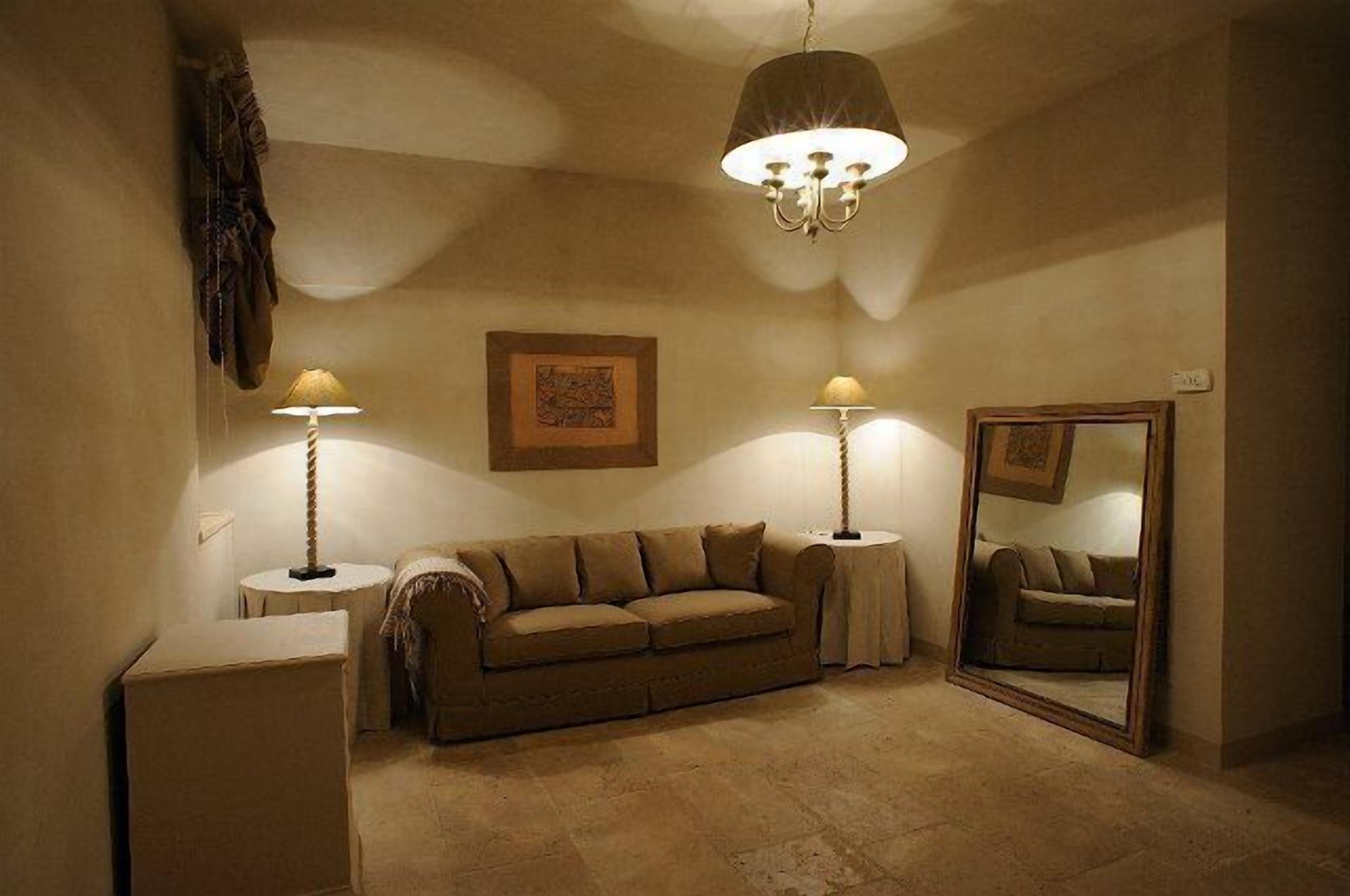 A cozy room with a beige sofa, two side tables with lamps, a large mirror, and a chandelier.