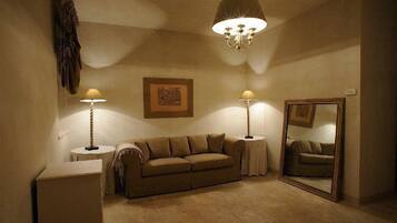A cozy room with a beige sofa, two side tables with lamps, a large mirror, and a chandelier.