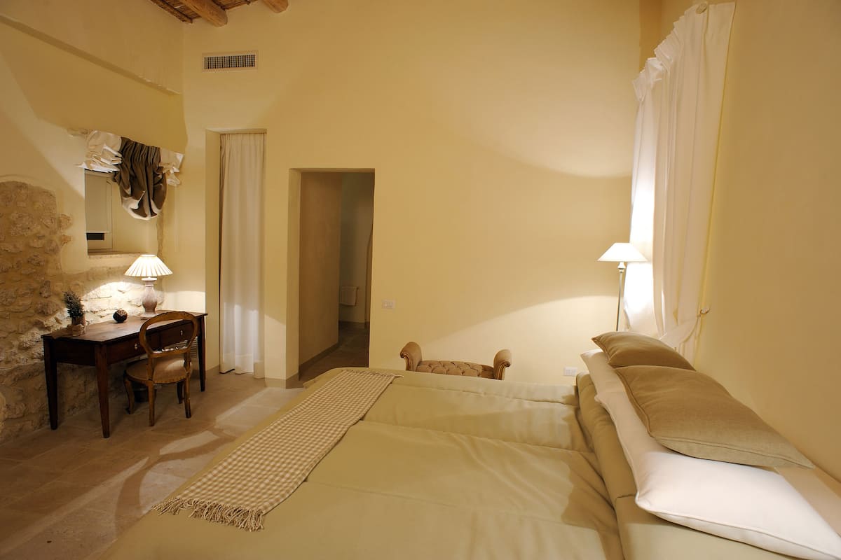 Um quarto com uma cama, uma escrivaninha com cadeira, uma luminária e um cão.