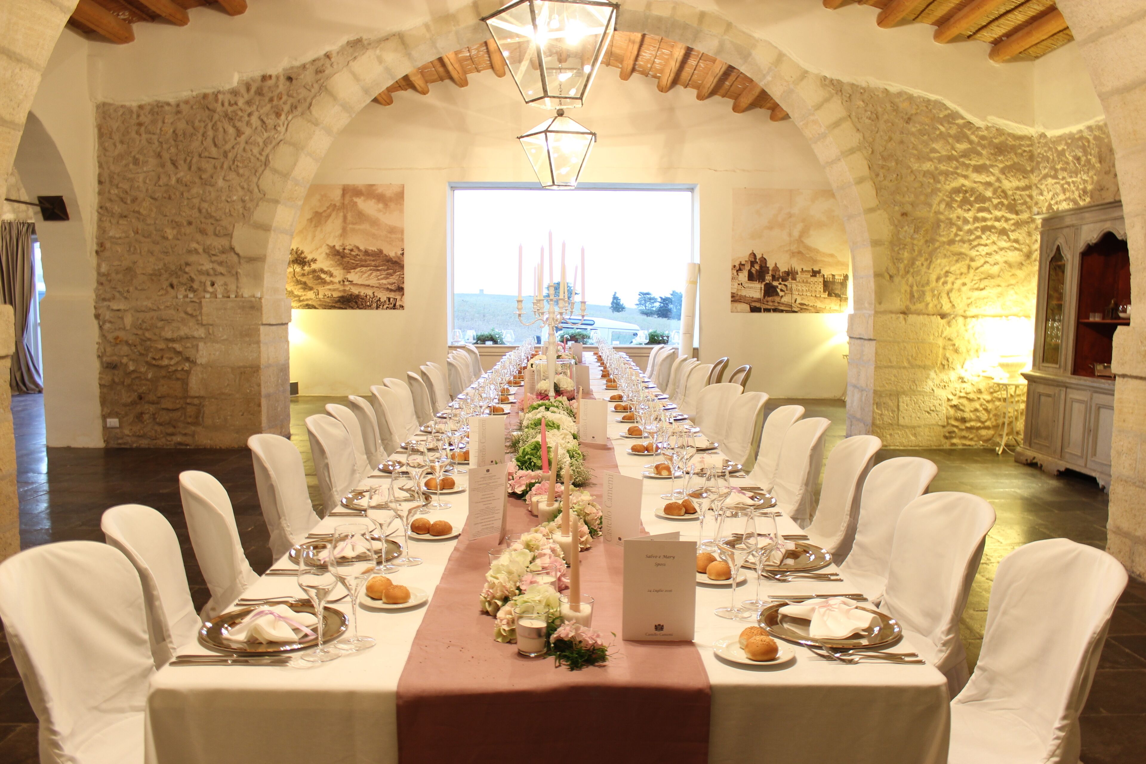A long dining table set for a formal event, with white chairs and a floral centerpiece.